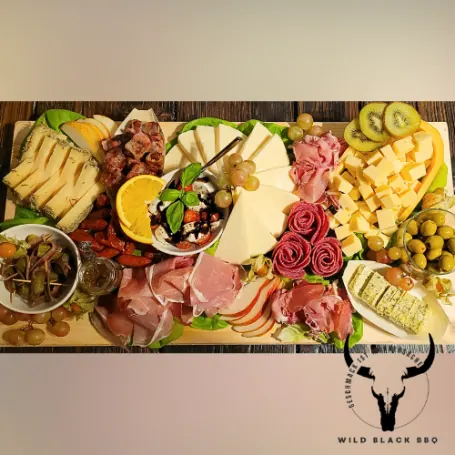 Üppig belegtes BBQ-Board mit Fleisch, Käse, Obst und Dips