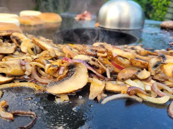 Fleischstreifen und Pilze brutzeln auf der heißen Plancha