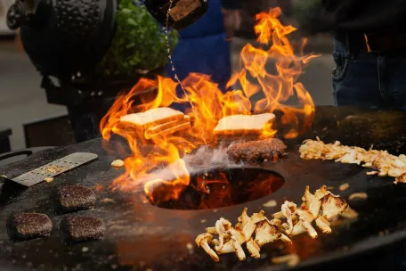 Offene Feuerstelle mit Flammen und Grillgut während eines Live-Cookings