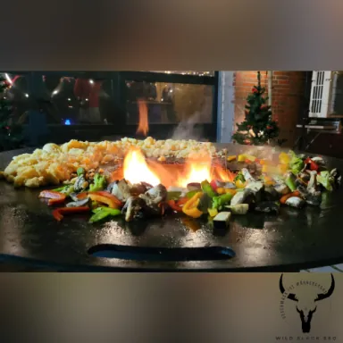 Große Plancha-Grillplatte mit Gemüse, Fleisch und züngelnden Flammen
